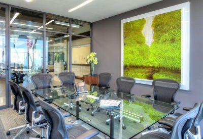 Glass-walled conference room featuring a large table, ergonomic black chairs, and nature wall art.