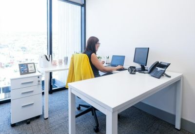 Private office suite with white desks, a yellow coat on a chair, and large windows.