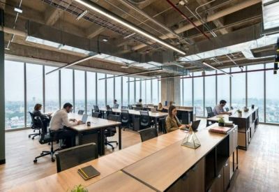Spacious open-plan office with long wooden desks and panoramic city views.