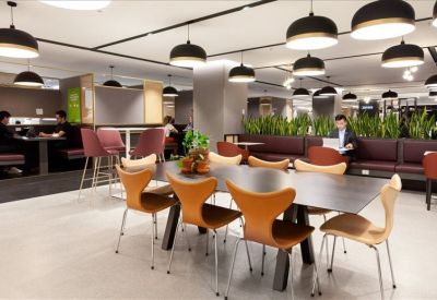 Modern communal lounge with stylish wood chairs, indoor plants, and warm overhead lighting.