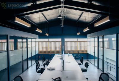 Spacious open-plan office with long white desks, ergonomic chairs, and industrial vaulted ceilings.
