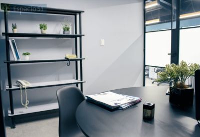 Meeting room featuring a round black table, modern shelving, and a glass-walled office entrance.