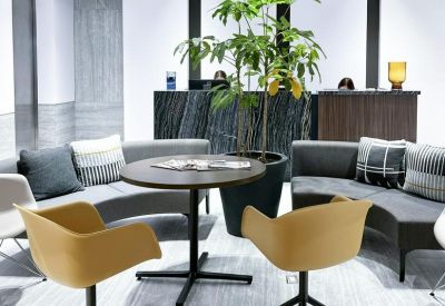 Modern lobby with yellow swivel chairs, a large plant, and a dark marble reception desk.