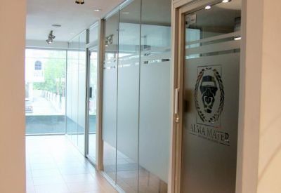 Bright office corridor featuring glass-walled suites and frosted door logos.