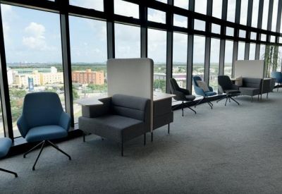 Modern lounge area with blue armchairs and privacy-screened sofas along a window wall.