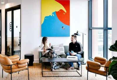 Bright lounge area featuring a large colorful abstract painting, tan leather chairs, and a glass coffee table.