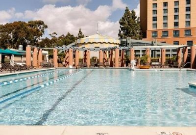 Outdoor lap pool with blue lounge umbrellas and a multi-story hotel building in the background.