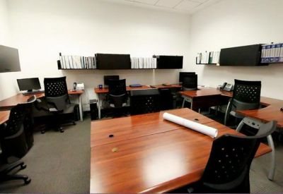 Shared workspace with multiple wooden desks and black ergonomic chairs.