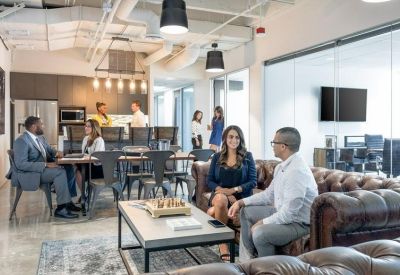 Spacious breakout area with leather sofas, coffee tables, and a kitchen in the background.
