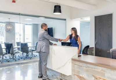 A man in a suit shaking hands with a receptionist at a marble front desk.