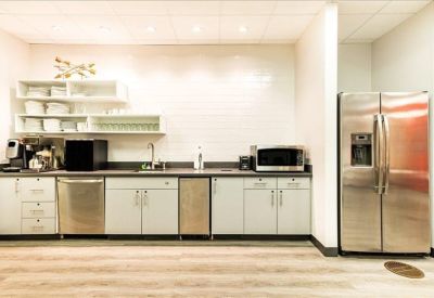Bright office kitchen area with stainless steel appliances and white cabinetry.