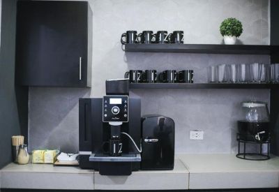 Communal kitchen area with a professional coffee machine and black mugs.