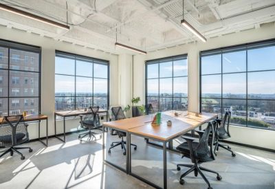 Sunlit coworking space with rows of ergonomic chairs and large industrial-style windows.