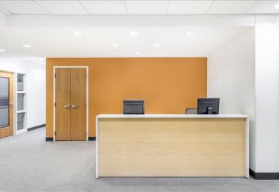 Minimalist reception area with a light wood front desk and an orange accent wall.