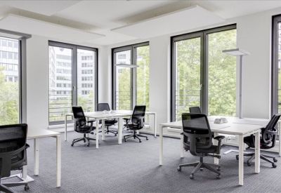 Bright open-plan office with white desks and black ergonomic chairs near large windows.
