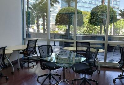Small meeting area with a glass table and ergonomic mesh chairs by a large window.