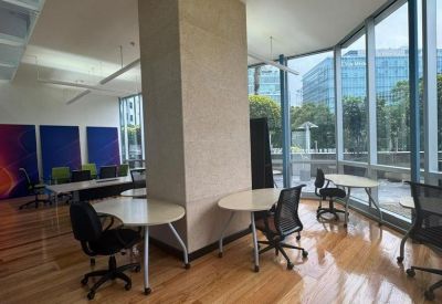 Spacious sunlit coworking area with wooden floors and city views through floor-to-ceiling windows.