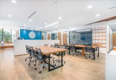 Spacious coworking area featuring multiple wooden tables and a blue accent wall with a large clock.