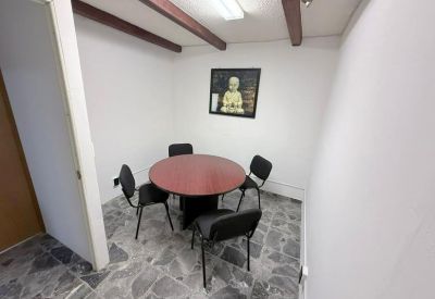 Meeting room with a round wooden table, four black chairs, and stone-patterned tile flooring.