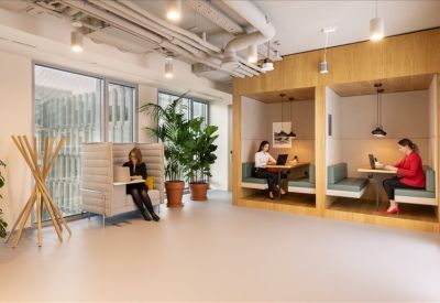 Modern lounge area featuring wooden work booths, integrated seating, and large potted plants.