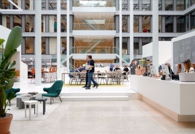 Bright, multi-story open lobby with a white reception desk and green lounge chairs.