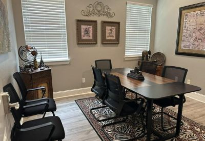 Meeting room with a central wooden table, black mesh chairs, and window blinds.