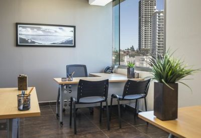 Bright corner office with wooden desks, ergonomic chairs, and a large window overlooking skyscrapers.