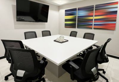 Modern conference room with a large white square table, black mesh chairs, and vibrant abstract art.