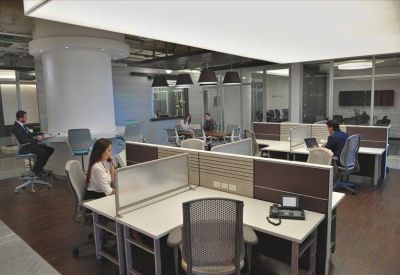 Open-plan office with multiple workstations, ergonomic chairs, and large windows.