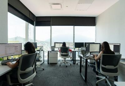 Open-plan workspace with multiple desks and floor-to-ceiling windows.