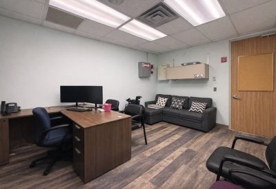 Spacious office suite with wood-look flooring, a large desk, and a comfortable gray sectional sofa.