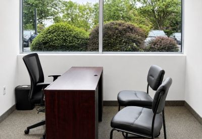 Bright private office featuring a large window with greenery views and visitor seating.