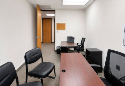 Compact two-person meeting room with dark wood desks and an open door to a hallway.