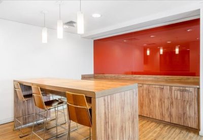 Breakout area with a large wooden high-top table and a vibrant red glass feature wall.