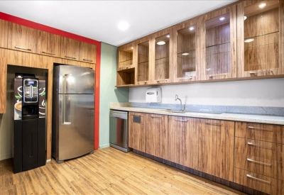 Modern office kitchen with wood-grain cabinets, stainless steel appliances, and red accent wall.