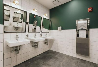 Modern restroom with three white sinks, dark green walls, and large black-framed mirrors.