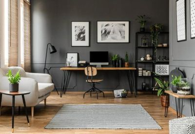 Modern home-style office with grey walls, a wooden desk, and a light grey sofa.