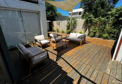 Sunny outdoor deck area with grey lounge furniture and wooden flooring.