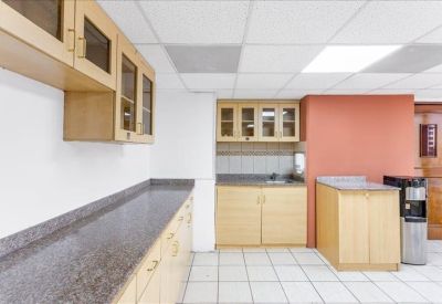 Office kitchen area with light wood cabinetry and grey granite countertops.