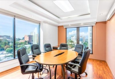 Oval wood boardroom table with black leather chairs and large windows.