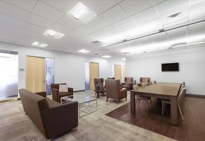Modern communal lounge area with brown leather armchairs, a sofa, and a long wooden table.