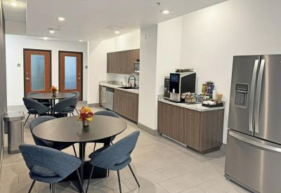 Communal kitchen and break area with wood cabinetry, stainless steel fridge, and dining tables.