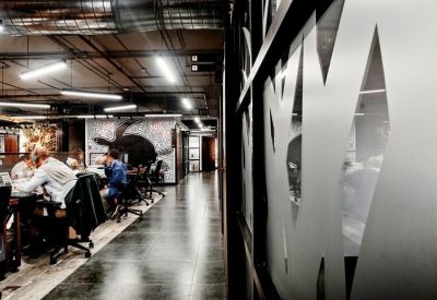 Modern office corridor with frosted glass partitions and people working at collaborative desks.