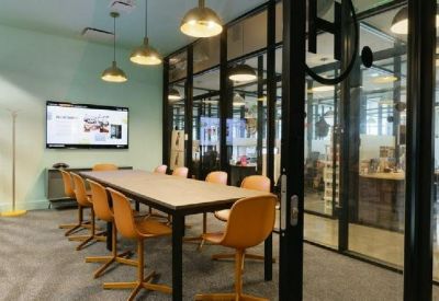 Glass-walled meeting room with a light wood table, tan chairs, and modern pendant lamps.