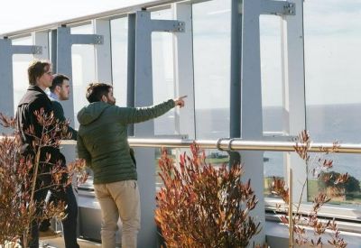 People standing on an outdoor balcony overlooking the ocean.