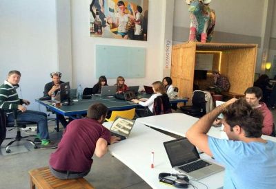 Casual workspace with people working at large tables and a blue ping pong table.
