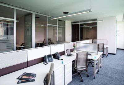 Open-plan office with white workstations, ergonomic chairs, and glass-walled private suites.