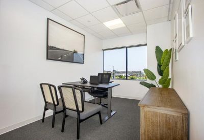 Private office suite with a dark desk, guest chairs, and a large window.