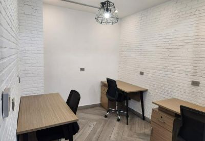 Minimalist office space with wooden desks and black task chairs against white brick walls.