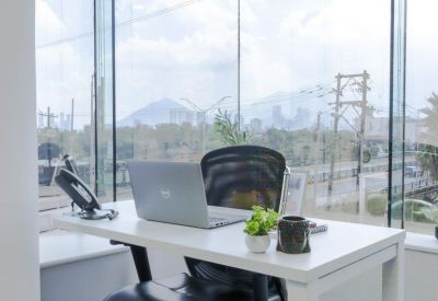 Bright private corner office with a white desk, laptop, and floor-to-ceiling city views.